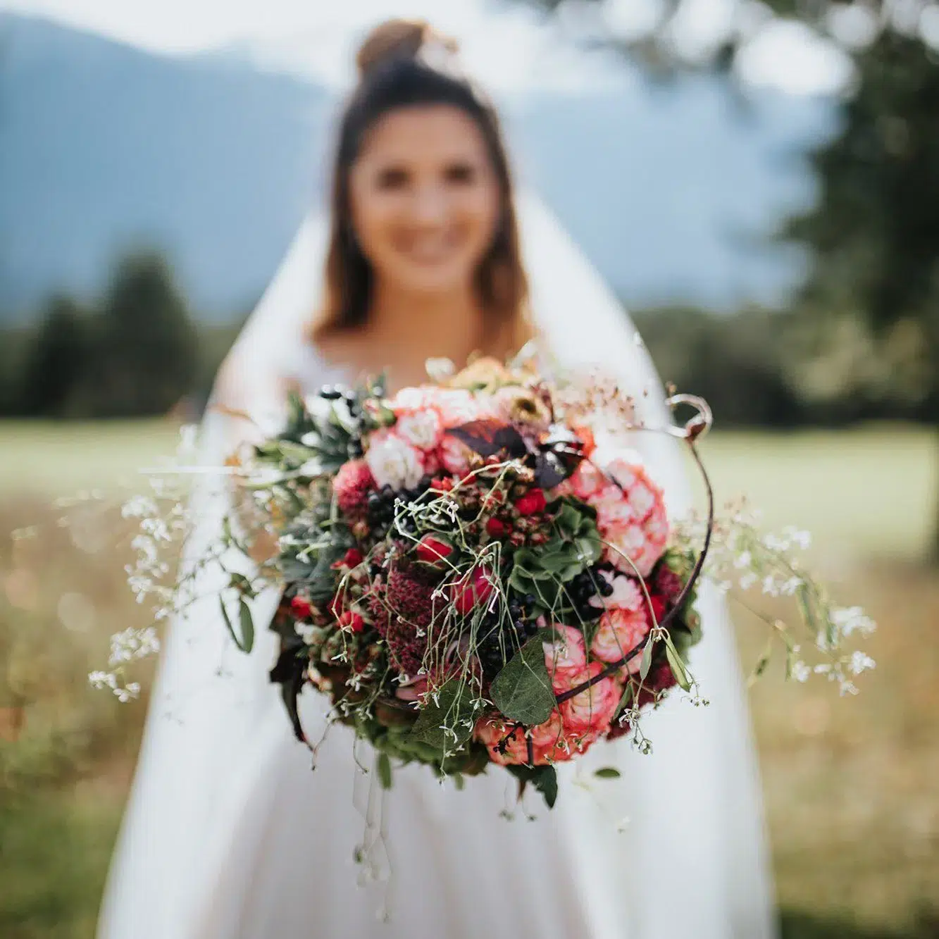 Braut in weißem Kleid mit buntem Blumenstrauß im Freien im malerischen Ötztal, Hintergrund unscharf.