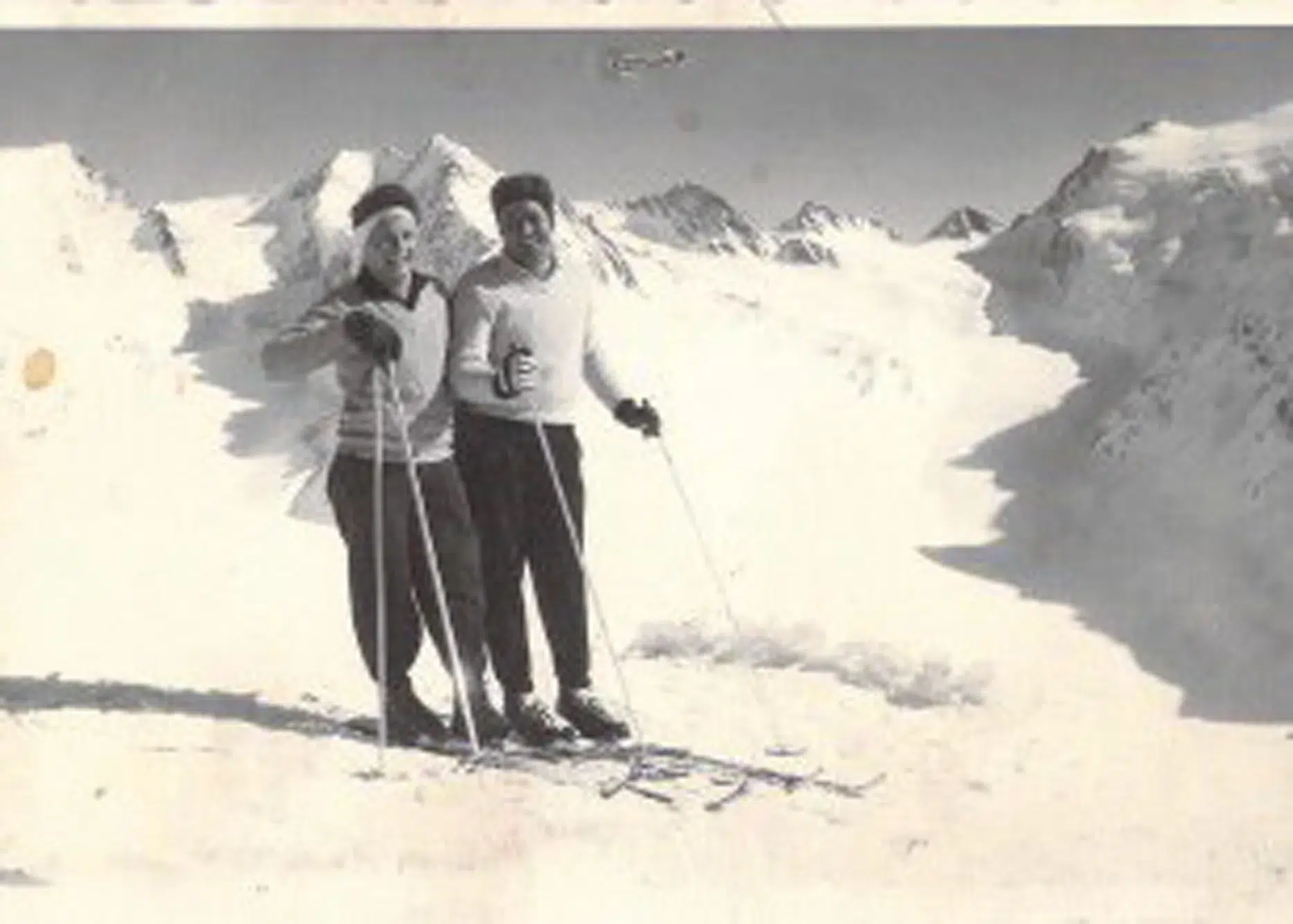 Zwei Personen stehen auf Skiern in den verschneiten Ötztaler Bergen und lächeln in die Kamera.