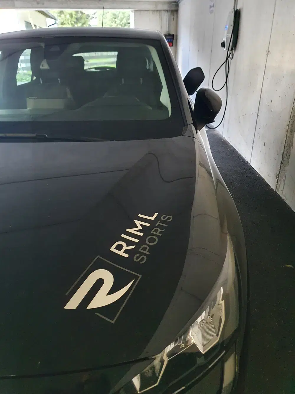 Schwarzes Auto mit RML Sports-Logo, geparkt neben einer Ötztaler Wandtankstelle.