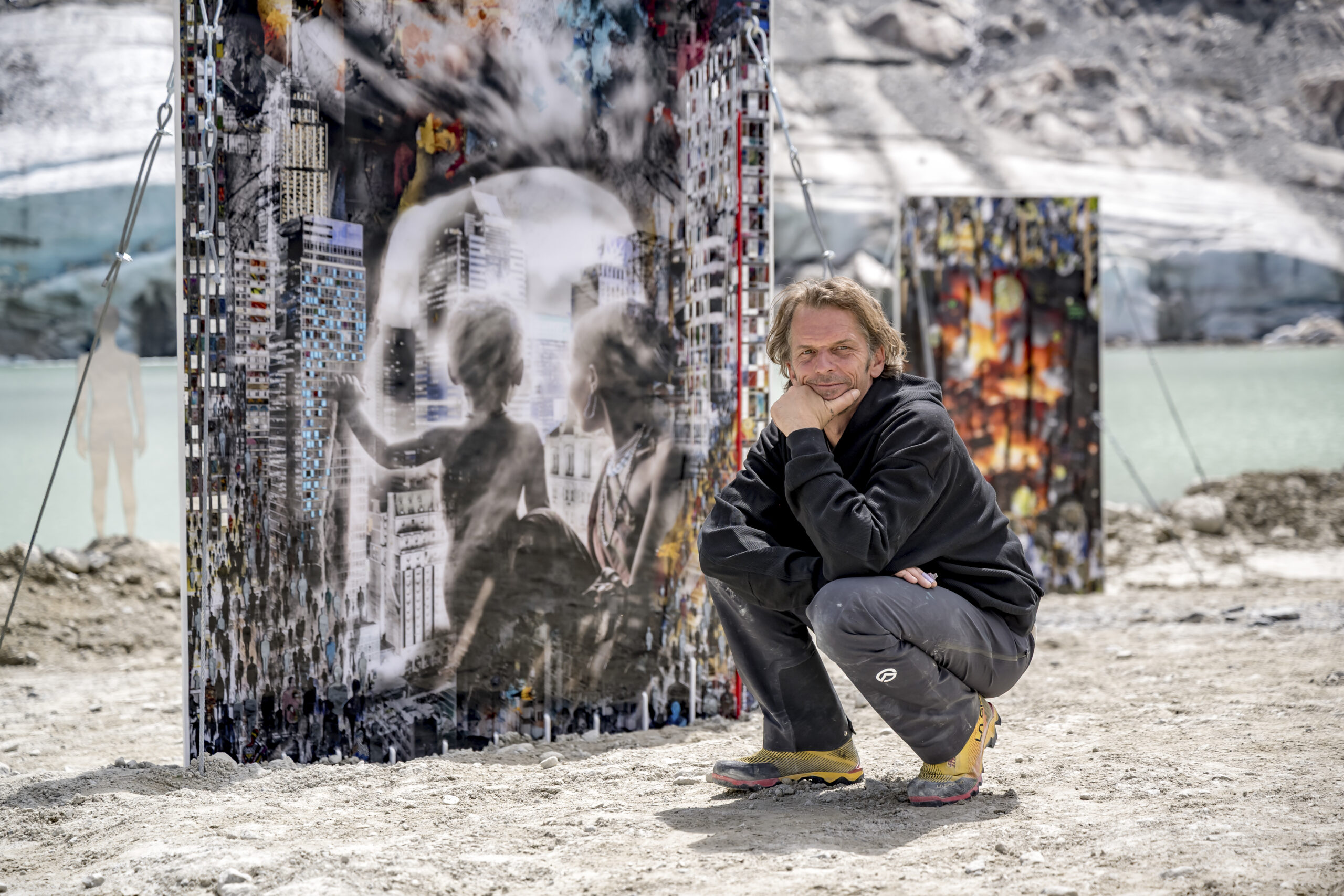 Ein Mann hockt neben bunten Kunsttafeln im Freien in der Nähe des Ötztaler Wassers und des felsigen Geländes.
