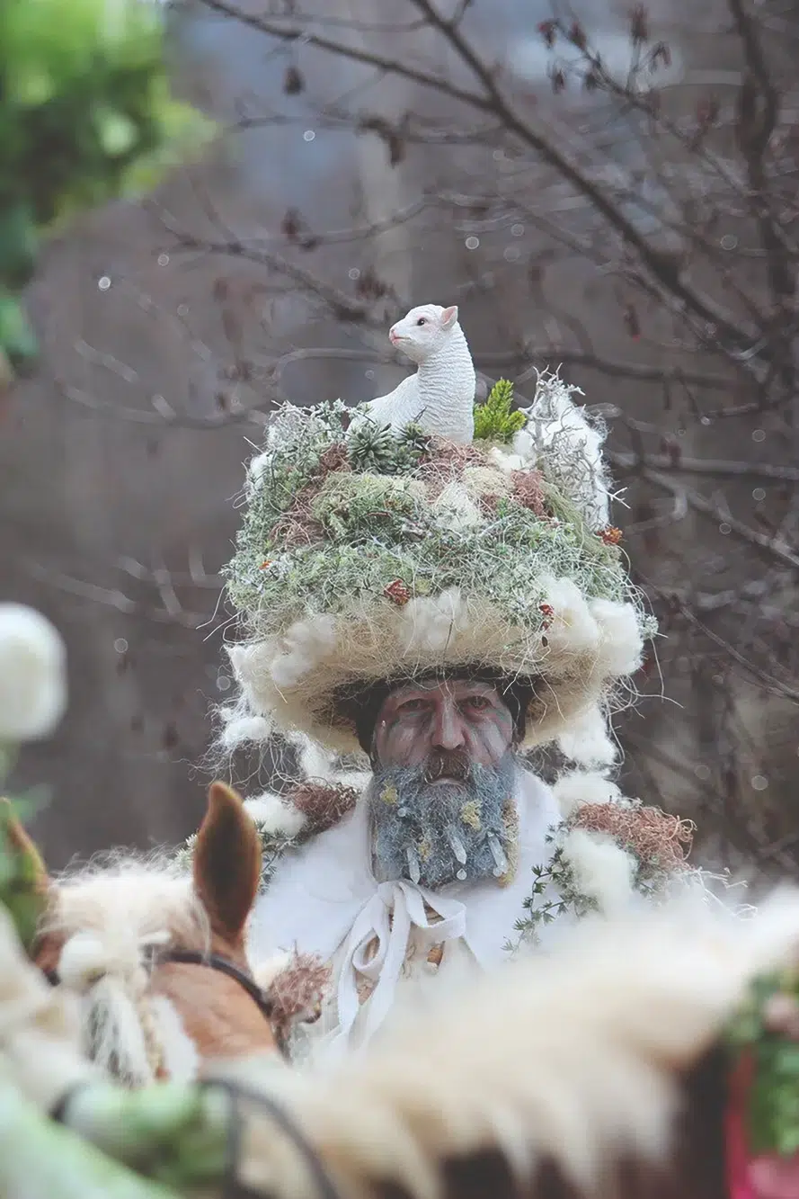 Person in einer vom Ötztal inspirierten Naturtracht mit einem großen Hut und einer weißen Tierfigur auf dem Kopf.