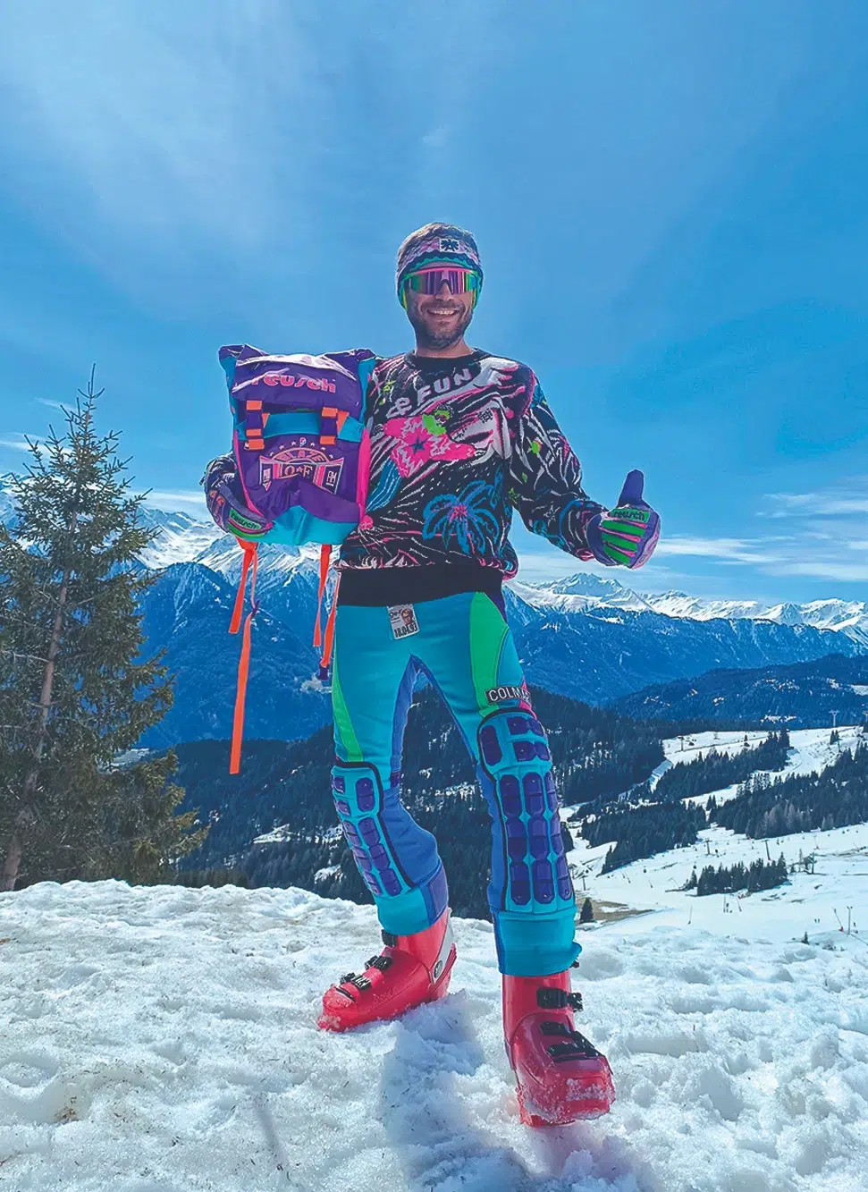 Person in bunter Skikleidung posiert auf einem verschneiten Ötztaler Berg mit blauem Himmel und fernen Gipfeln.