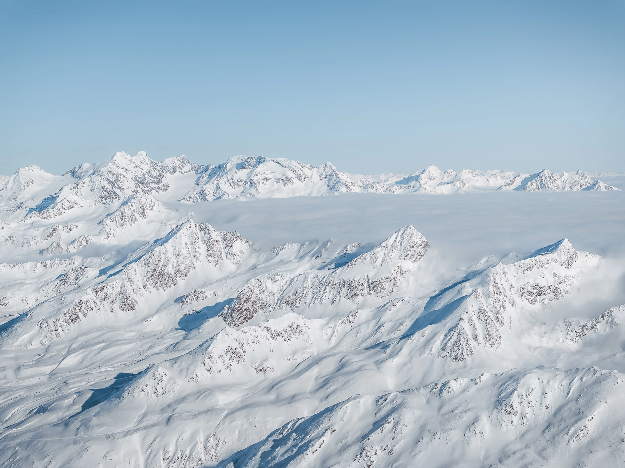 Schneebedeckte Ötztaler Berggipfel unter einem klaren blauen Himmel mit niedrigen Wolken im Hintergrund.