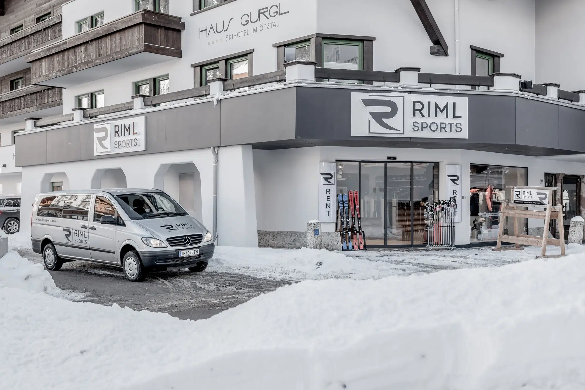 Eine verschneite Riml Sports-Filiale im Ötztal mit einem Lieferwagen und Skiern am Eingang.