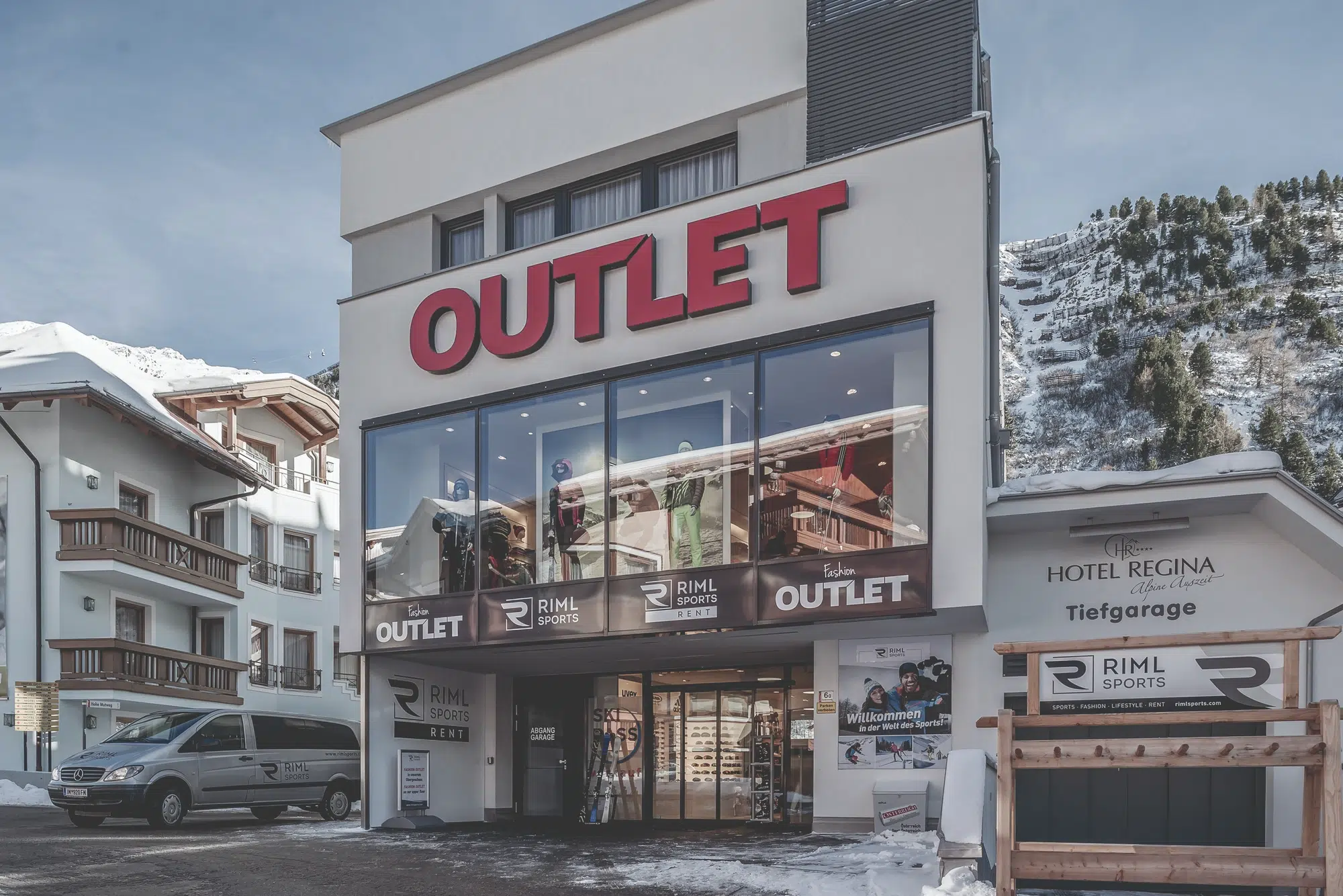 Modernes Ötztaler Outlet-Geschäft mit großem roten Schild, verschneiter Straße und Bergen im Hintergrund.