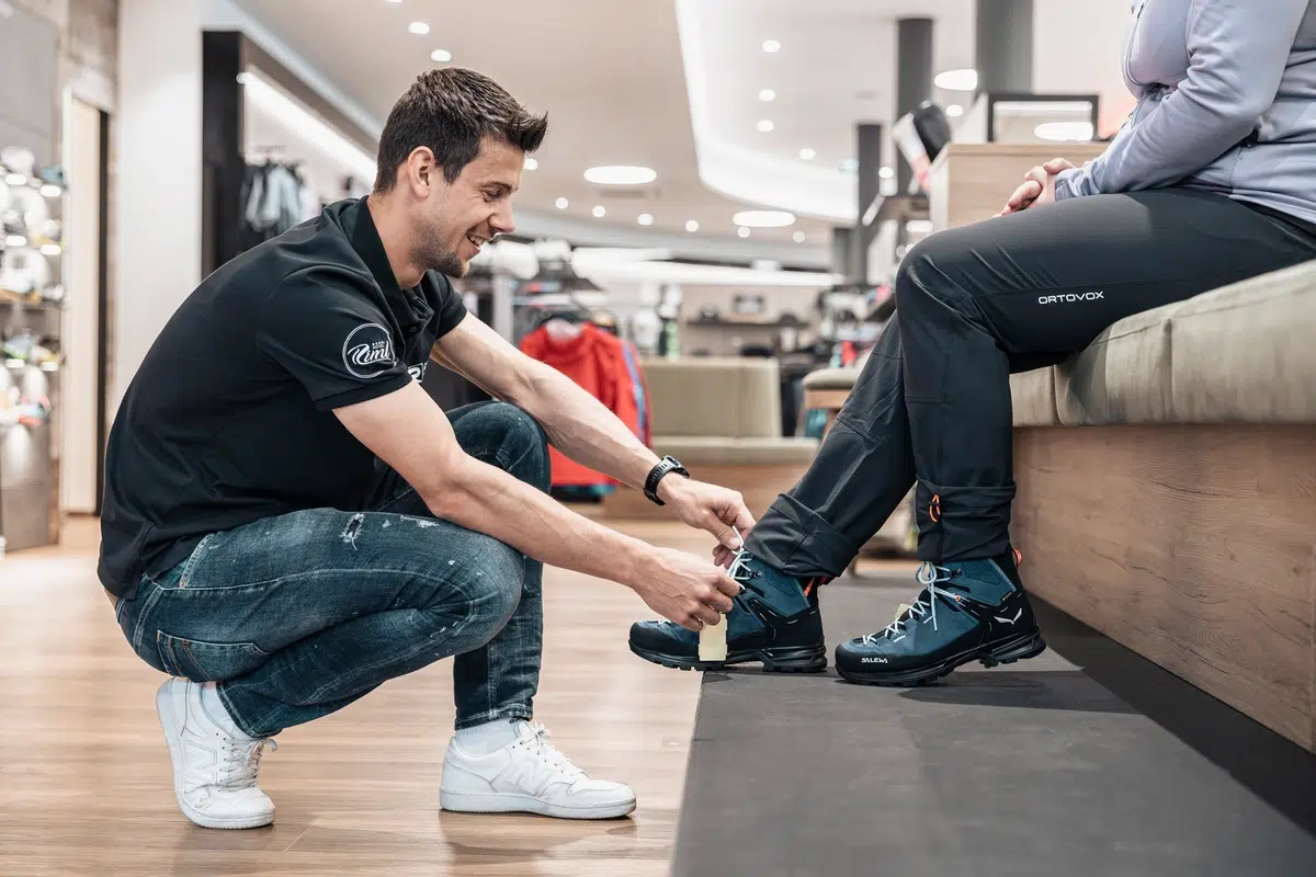 Ein Mann hilft einer sitzenden Person beim Anprobieren von Ötztaler Wanderschuhen in einem Schuhgeschäft.