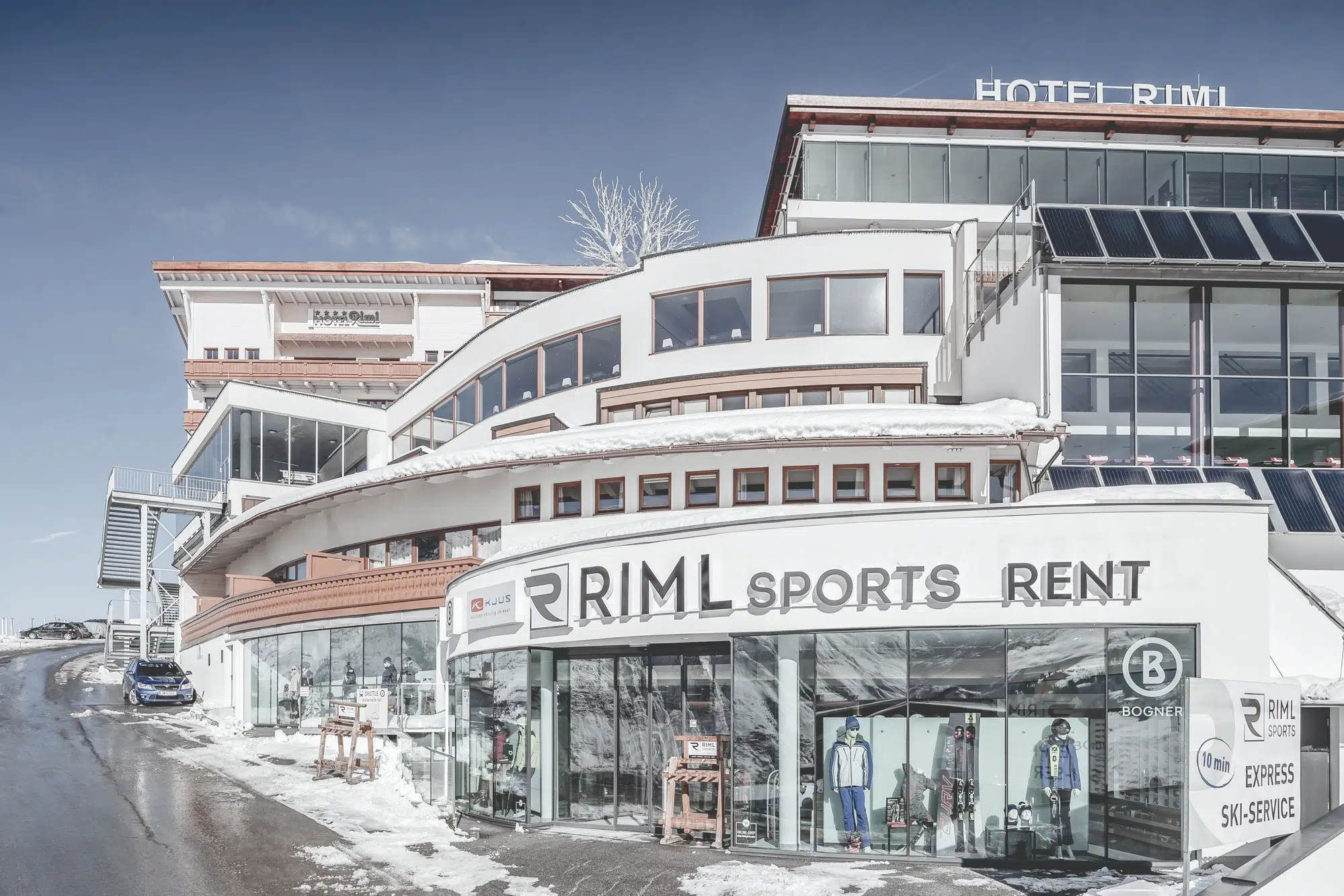 Gebogenes Gebäude mit RIML SPORTS RENT-Schild im Ötztal, verschneiter Boden und ausgestellte Skiausrüstung.