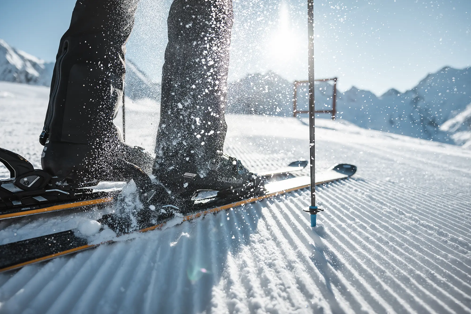 Nahaufnahme von Skischuhen und Skiern von Skifahrern auf frischem Ötztaler Schnee mit Bergen im Hintergrund.
