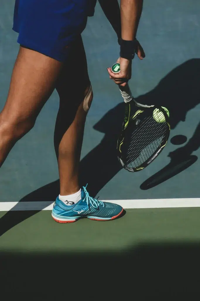 Person in blauen Schuhen, die einen Tennisschläger in der Hand hält, bereit zum Spiel auf einem Ötztaler Tennisplatz.