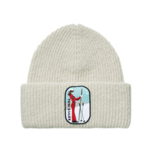 Cremefarbene Strickmütze mit Skifahrerinnen-Aufnäher und Ötztaler TOM SAUER-Inspiration auf dem vorderen Bündchen.