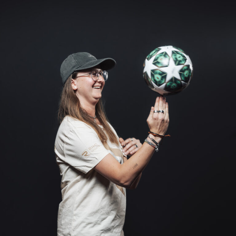 Eine lächelnde Person, die einen Fußball dreht und damit Jobs und Teamgeist vor einem dunklen Hintergrund demonstriert.