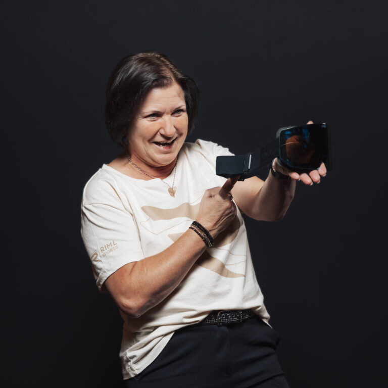 Lächelnde Frau im weißen Hemd, die einen Barcode-Scanner hält und darauf zeigt, vor einem schwarzen Hintergrund.