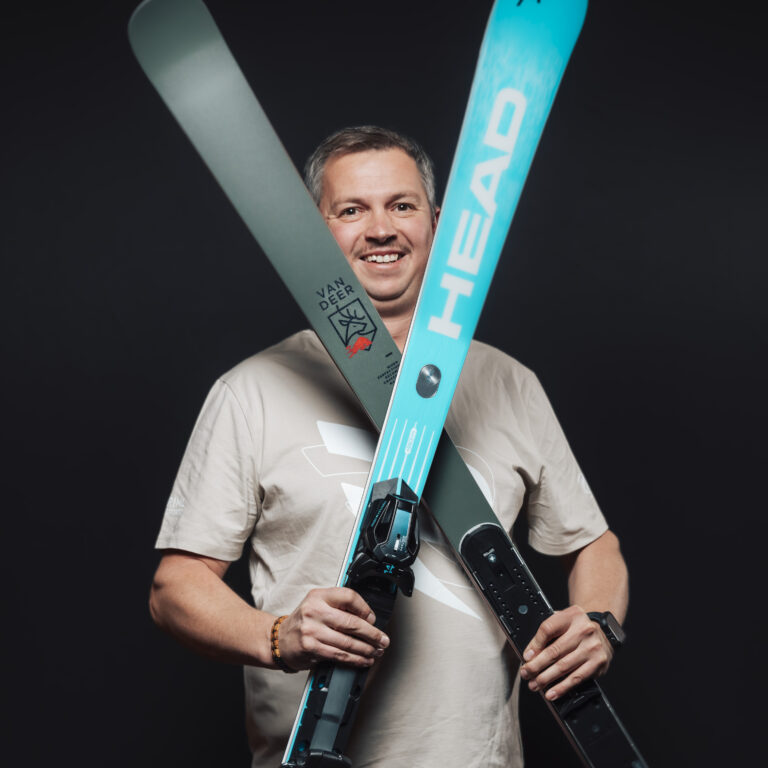 Lächelnder Mann mit gekreuzten Skiern, der vor einem schwarzen Hintergrund seinen Teamgeist demonstriert.