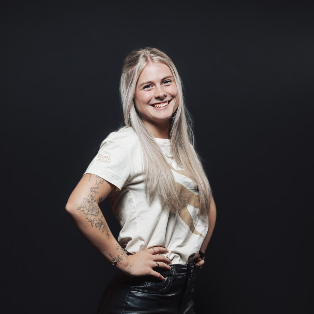 Smiling woman with long blonde hair and tattoos, posing as part of our Jobs & Team series.
