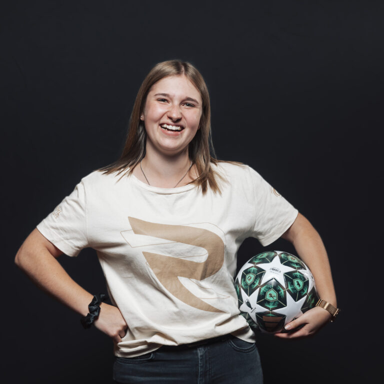 Lächelnde junge Frau mit einem Fußball in der Hand, bereit für Teamaufgaben vor einem schwarzen Hintergrund.