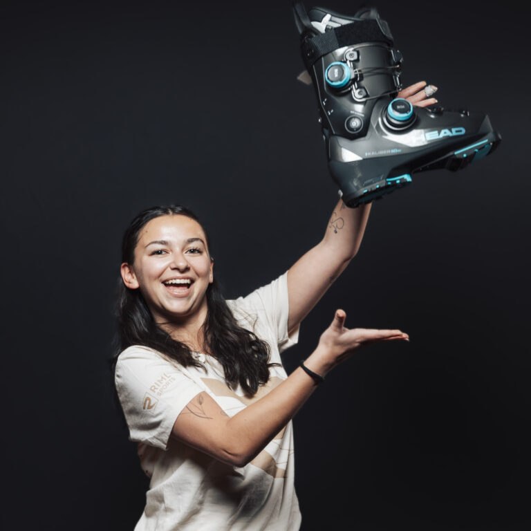 Eine lächelnde Frau, die einen großen schwarzen Skischuh hochhält, um unseren Jobs & Teamgeist zu zeigen.