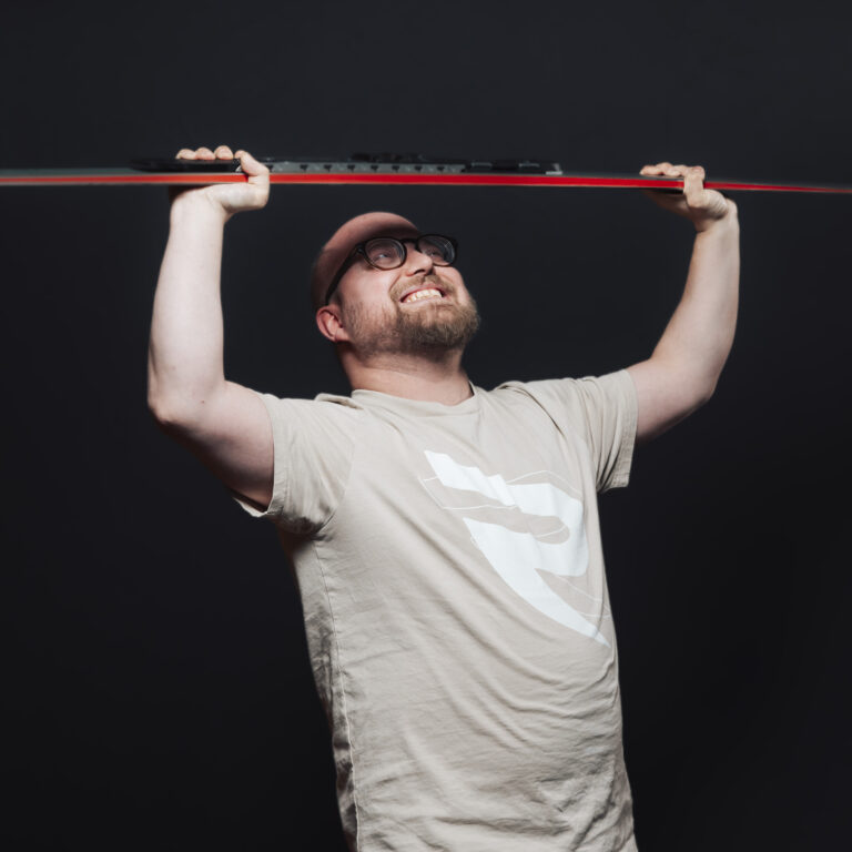 Ein lächelnder Mann mit Brille zelebriert Jobs und Teamgeist und hält ein rot-schwarzes Objekt in die Höhe.