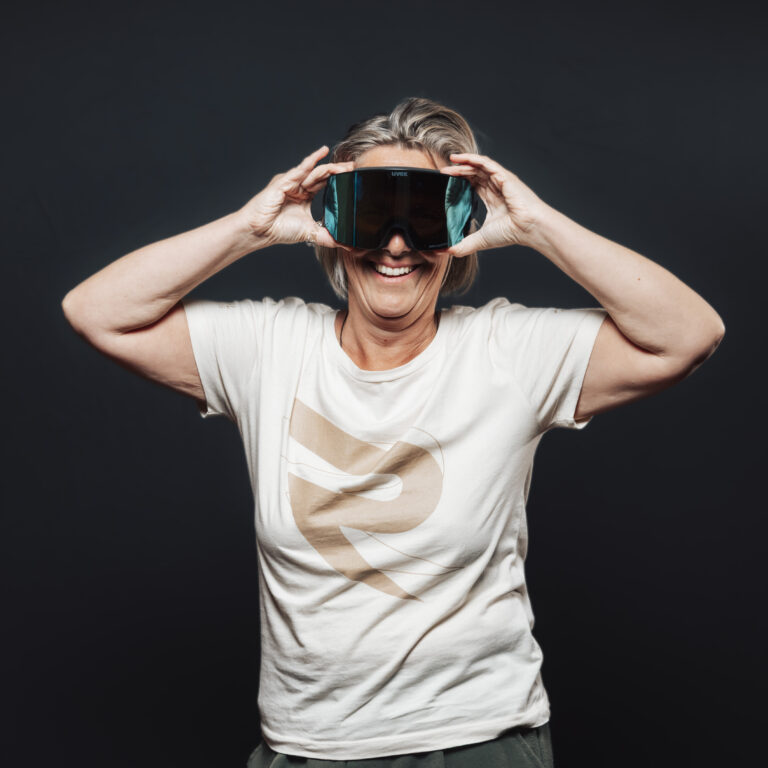 Ein lächelndes Teammitglied in einem weißen Hemd hält eine große Schutzbrille, die Jobs und Teamgeist einfängt.