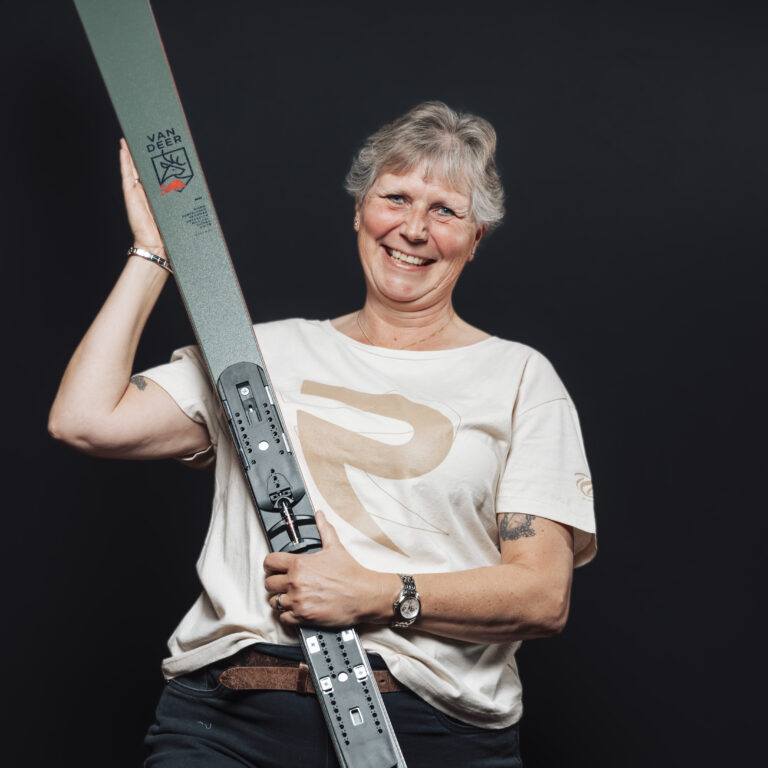 Lächelnde ältere Frau mit einem Ski in der Hand, die Teamgeist vor einem schwarzen Hintergrund verkörpert.