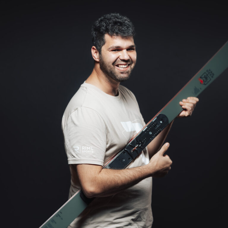 Ein lächelnder Mann in einem hellen Hemd mit einem Ski in der Hand, bereit für neue Jobs und Teamabenteuer.