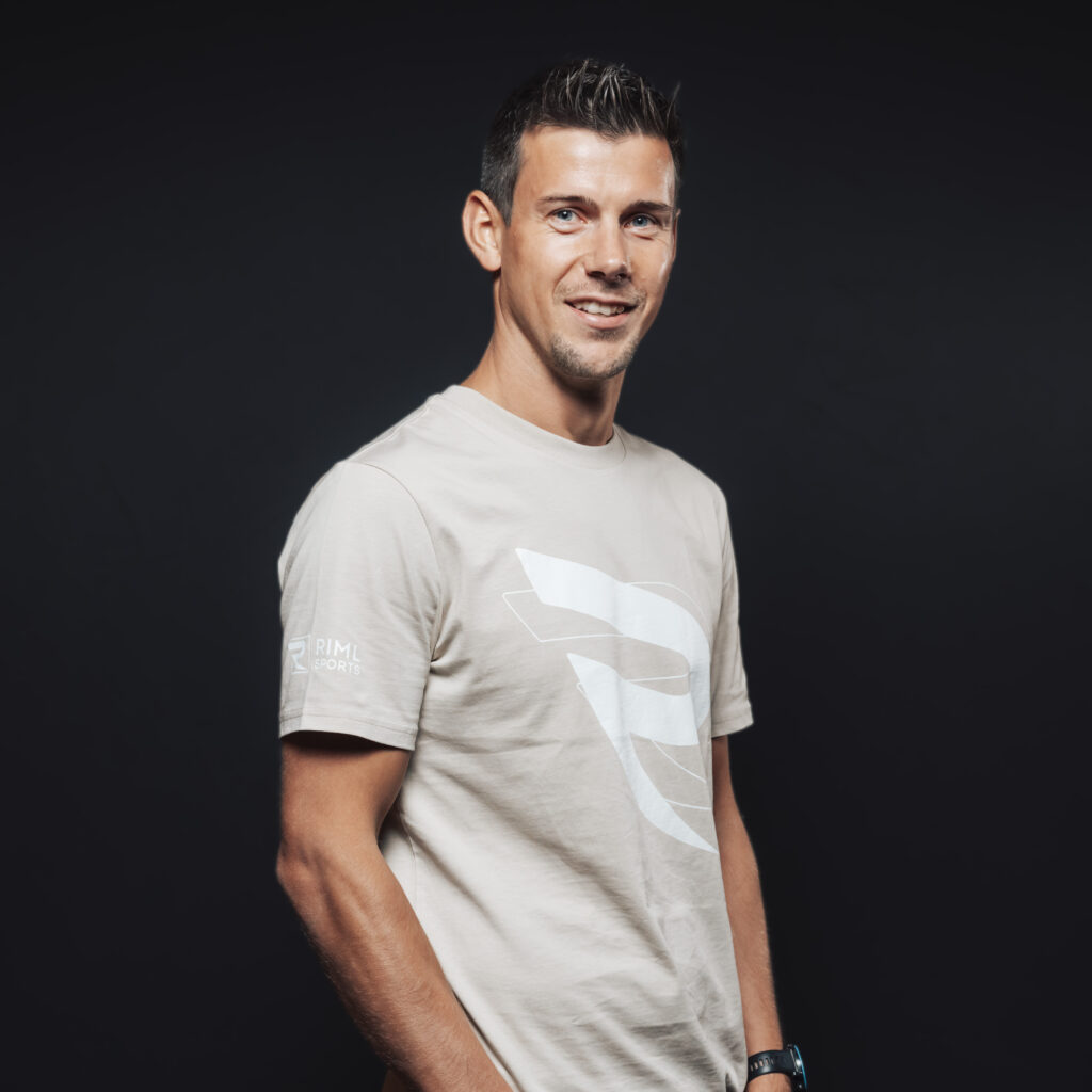 Man in a beige t-shirt smiling, representing Jobs & Team spirit against a dark background.