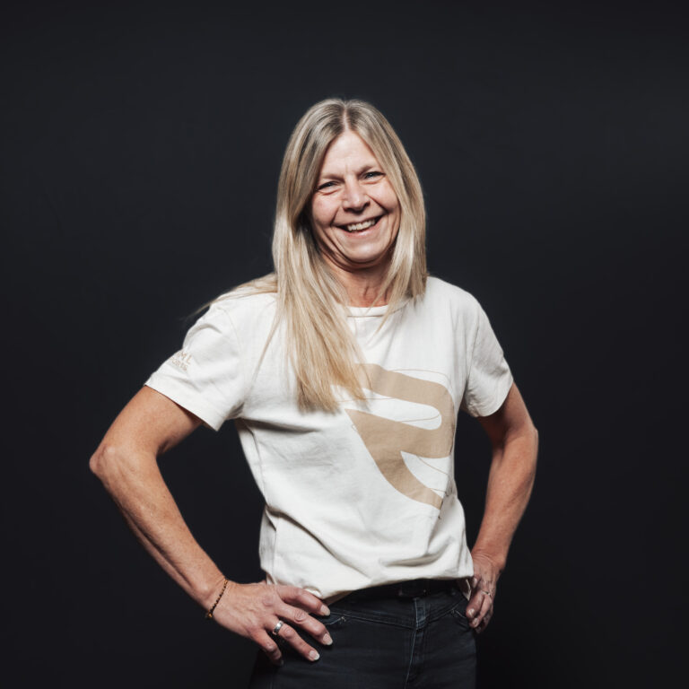 Lächelnde Frau mit langen blonden Haaren in einem weißen T-Shirt, perfekt für Jobs & Team-Profile.