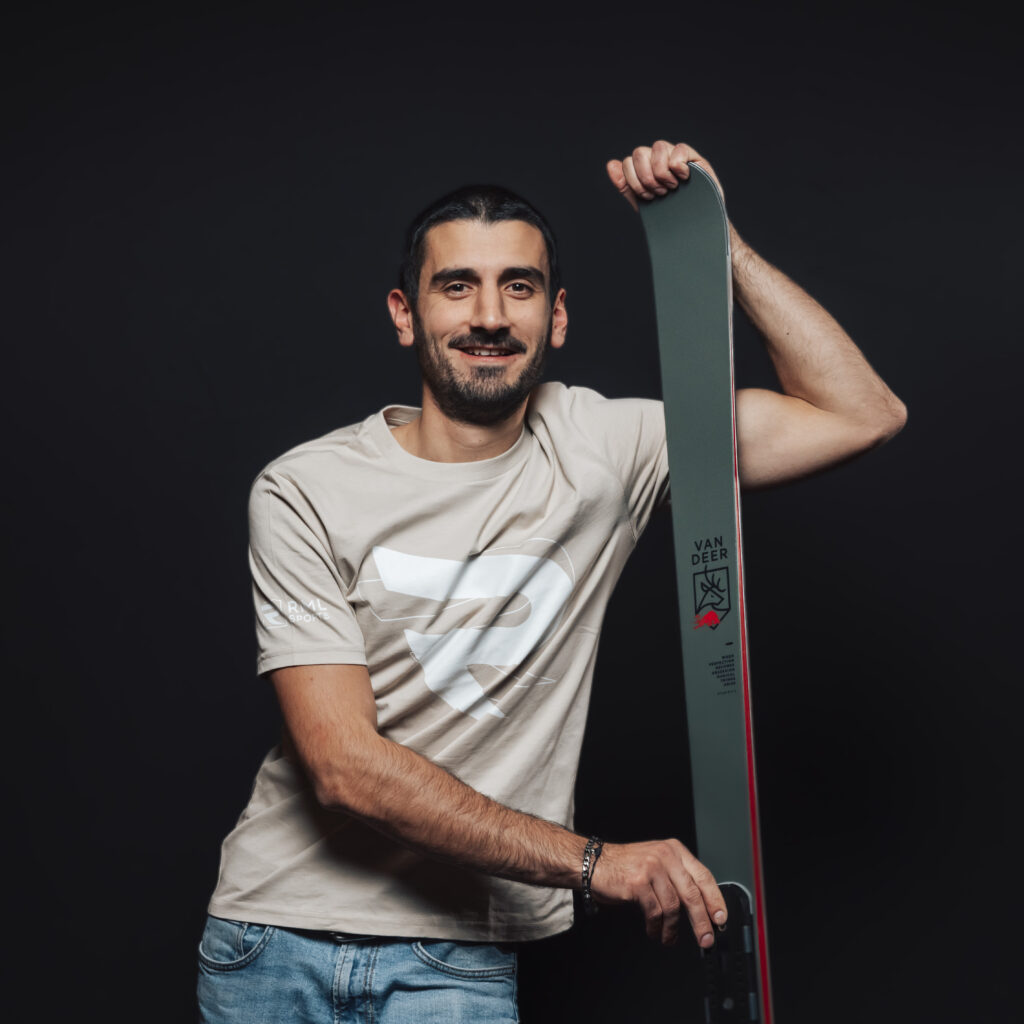 Man in a beige t-shirt holding a ski, ready for action—perfect for Jobs & Team profiles.