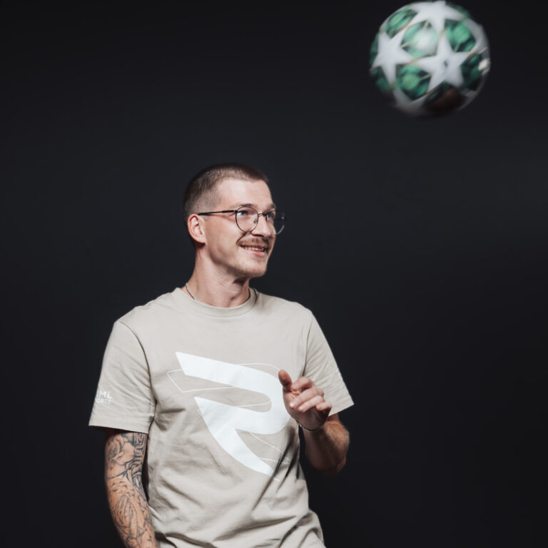 Ein lächelnder Mann mit Brille und T-Shirt, der zu unserem Team gehört, beobachtet einen Fußball in der Luft.