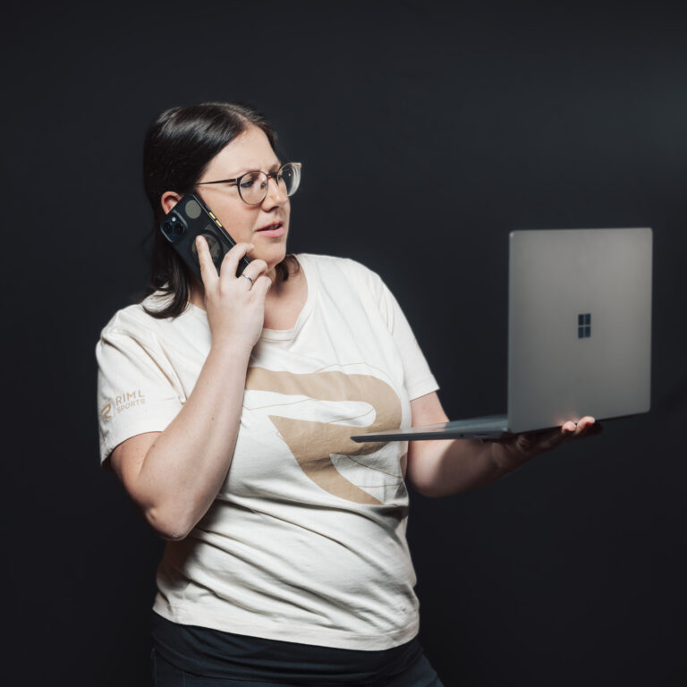 Eine Frau hält einen Laptop in der Hand und telefoniert, wobei sie sich auf Aufgaben und Teamarbeit konzentriert.