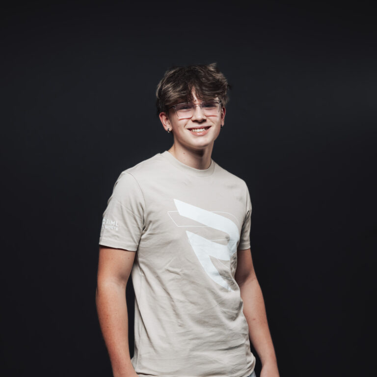 Junger Mann mit Brille, lächelnd, Teil unseres Jobs & Teams, in einem beigen T-Shirt, dunkler Hintergrund.