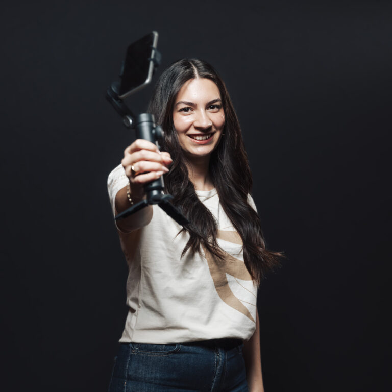 Lächelnde Frau, die ein Smartphone auf einem Stabilisator hält und Momente von Jobs & Team festhält.