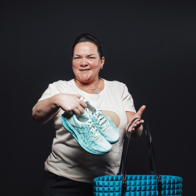 Lächelnde Frau mit türkisfarbenen Turnschuhen über einer Tasche, bereit für neue Jobs und Teamabenteuer.