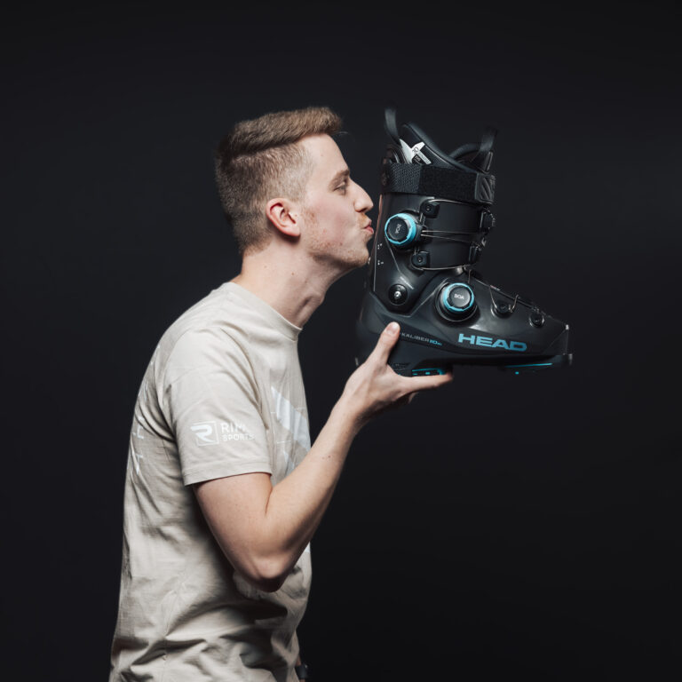 Ein Mann küsst einen schwarzen Skischuh vor einem dunklen Hintergrund, der den Teamgeist unterstreicht.